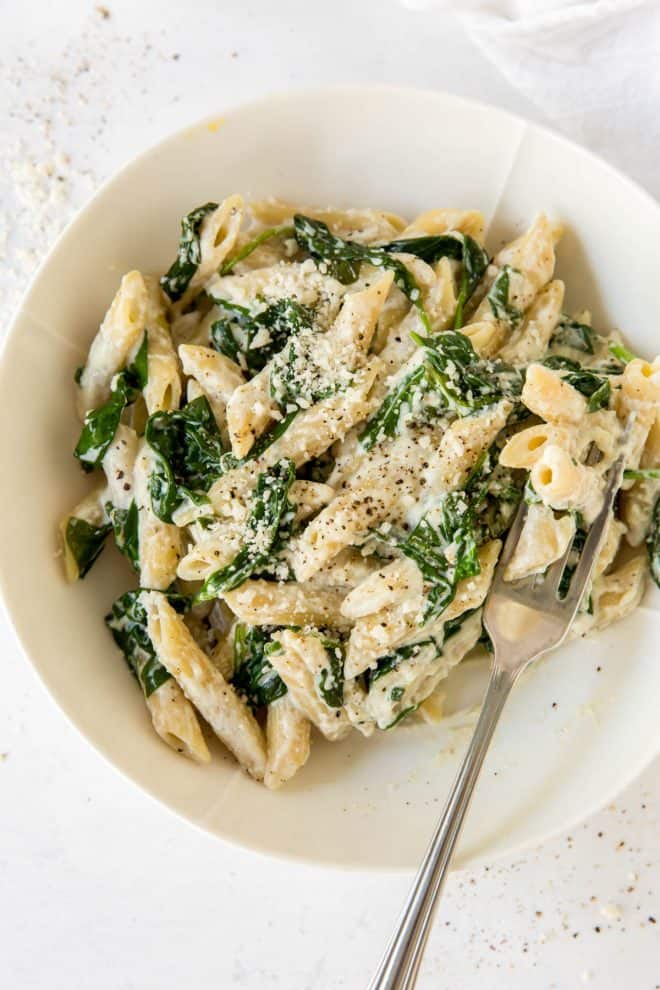 spinach and ricotta pasta in a white bowl with a fork