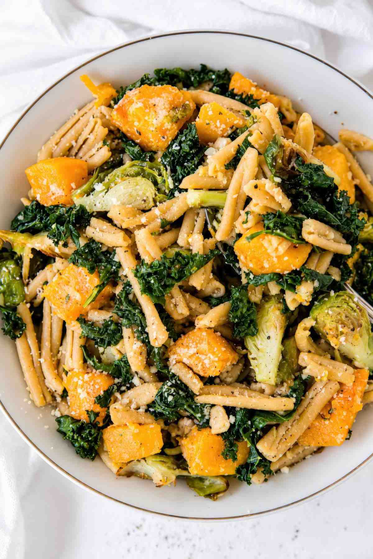 Overhead close-up of casarecce pasta tossed with butternut squash, kale, Brussels sprouts, and Parmesan.