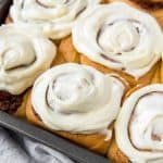 baked cinnamon rolls in a metal tin with cream cheese frosting on top