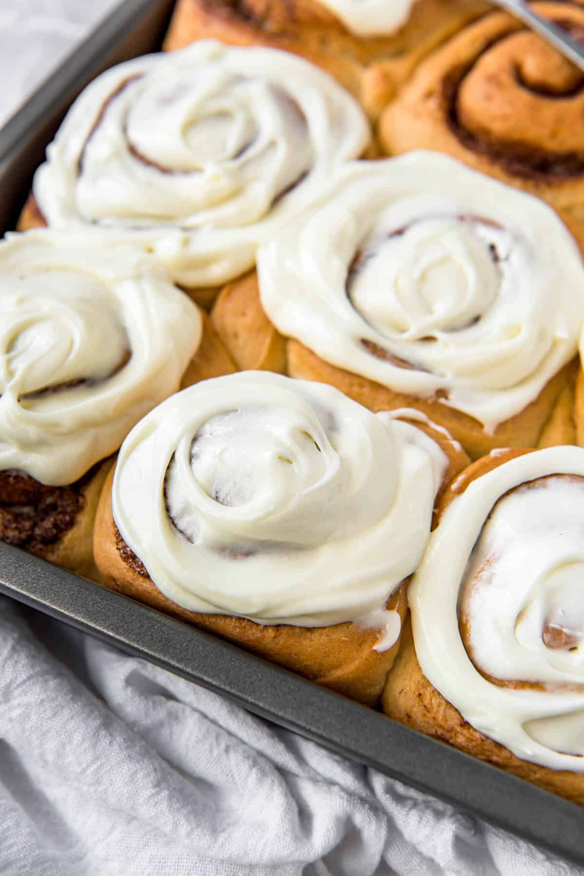 baked cinnamon rolls in a metal tin with cream cheese frosting on top