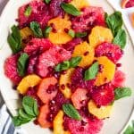 a white plate with citrus salad on top garnished with pomegranate seeds and fresh mint