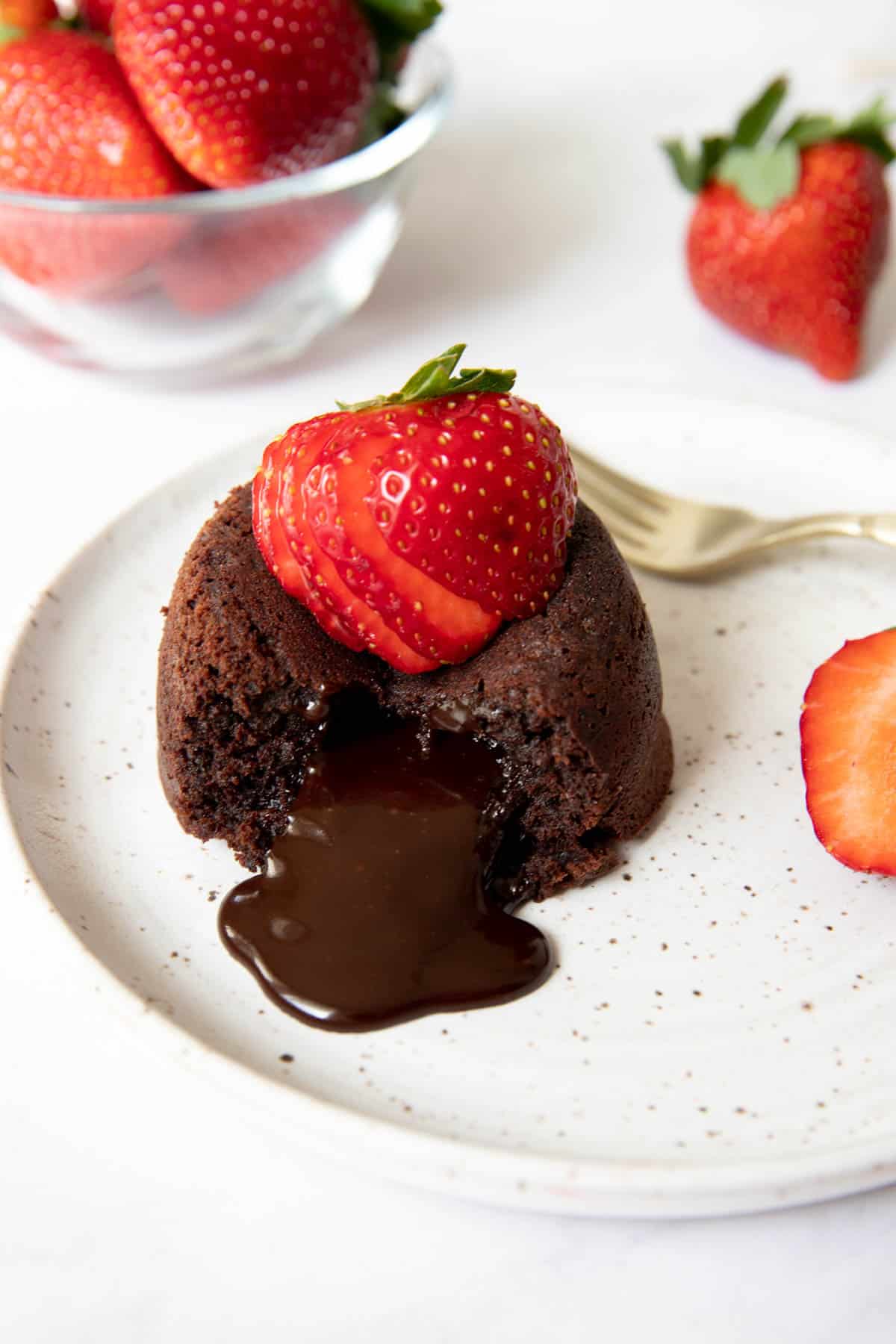 one lava cake sitting on a white plate with a sliced strawberry on top