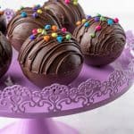 hot chocolate balls filled with hot cocoa sitting on a purple cake stand
