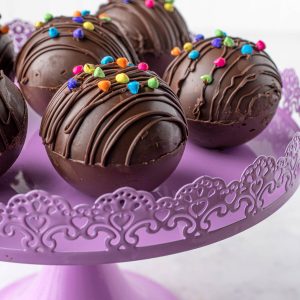 hot chocolate balls filled with hot cocoa sitting on a purple cake stand