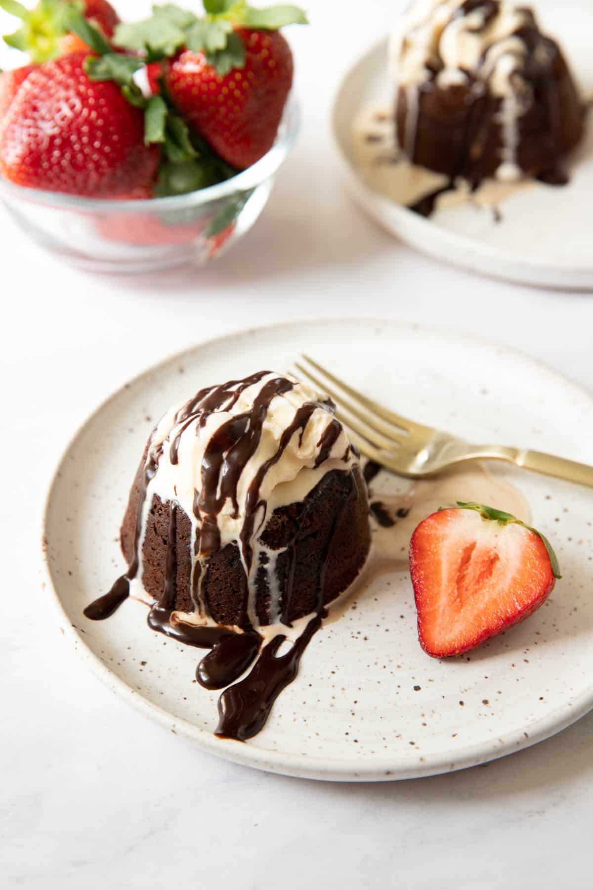 two molten lava cakes sitting on plates with scoop of vanilla ice cream and chocolate drizzle