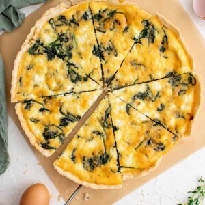 a spinach and feta quiche cut into 8 slices on a white table