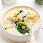 a bowl of tortellini soup sitting on a white table