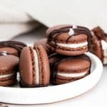 a stack of chocolate macarons sitting on a white plate