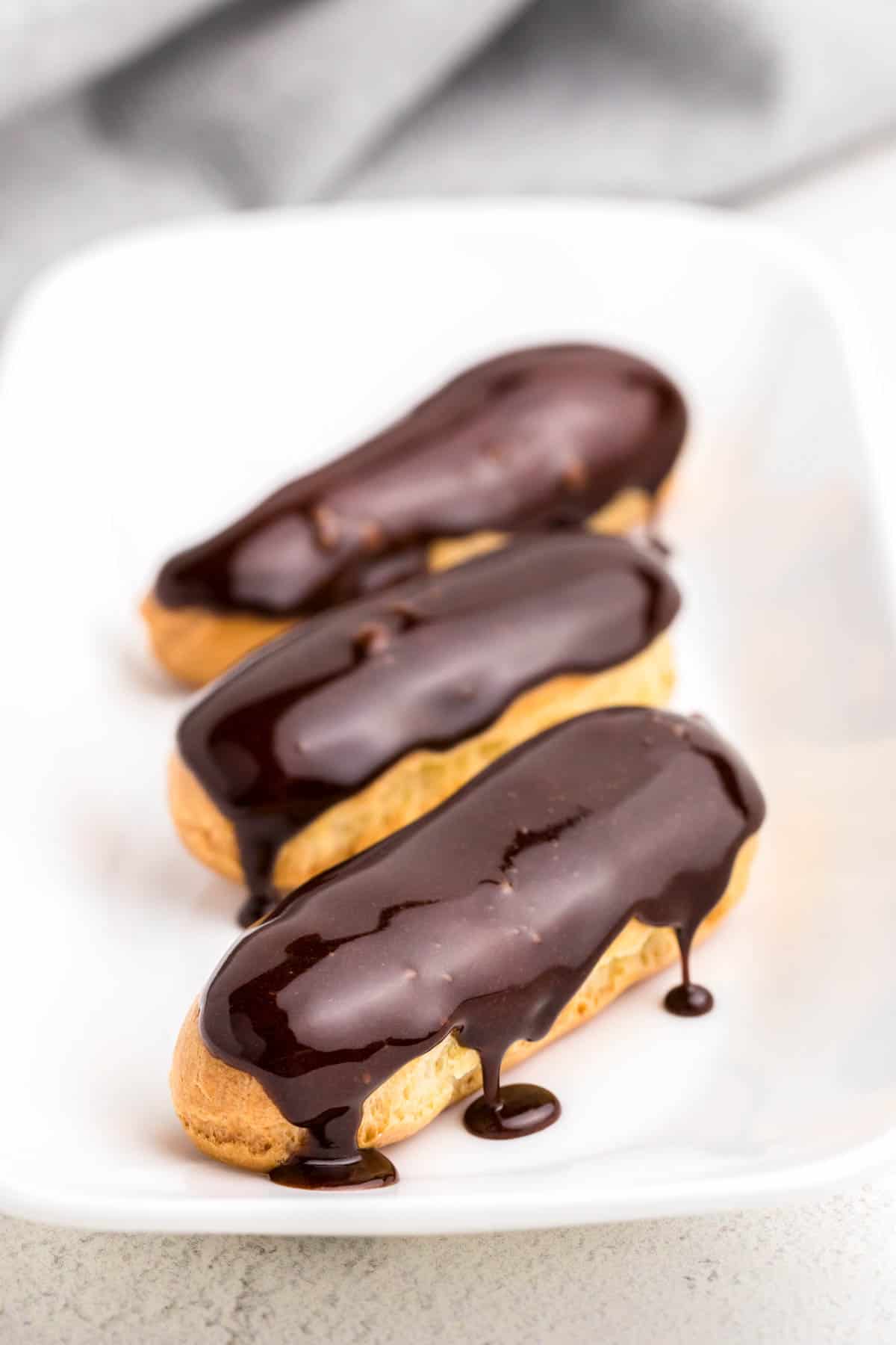 Three chocolate eclairs on a plate.