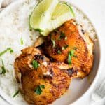 two chicken thighs on a plate with a side of rice and lime slices
