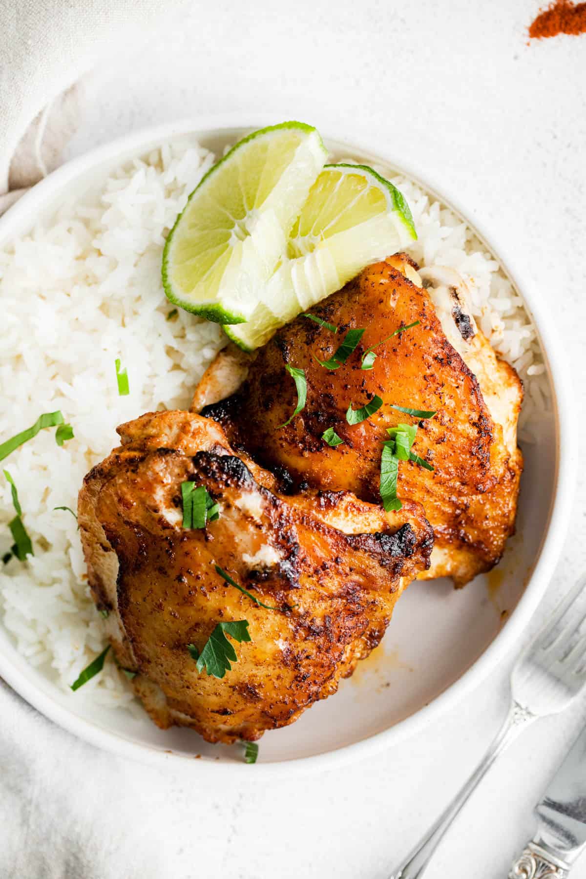 two chicken thighs on a plate with a side of rice and lime slices