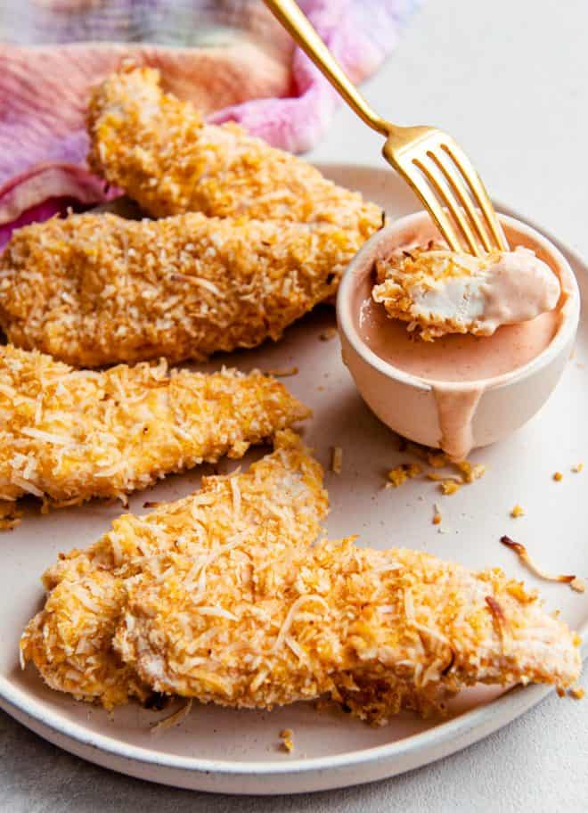 dipping a piece of coconut chicken tender into dip