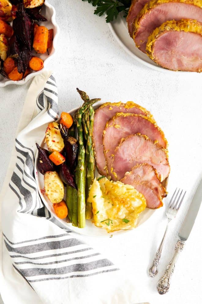 ham, scalloped potatoes, asparagus and root vegetables on a white plate