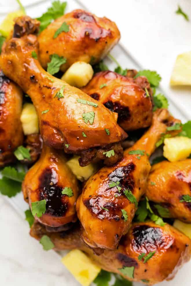 Hawaiian Pineapple drumsticks piled on a white plate, topped with cilantro and pineapple.