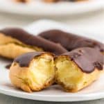Three eclairs on a plate, one cut in half to show the vanilla cream center.