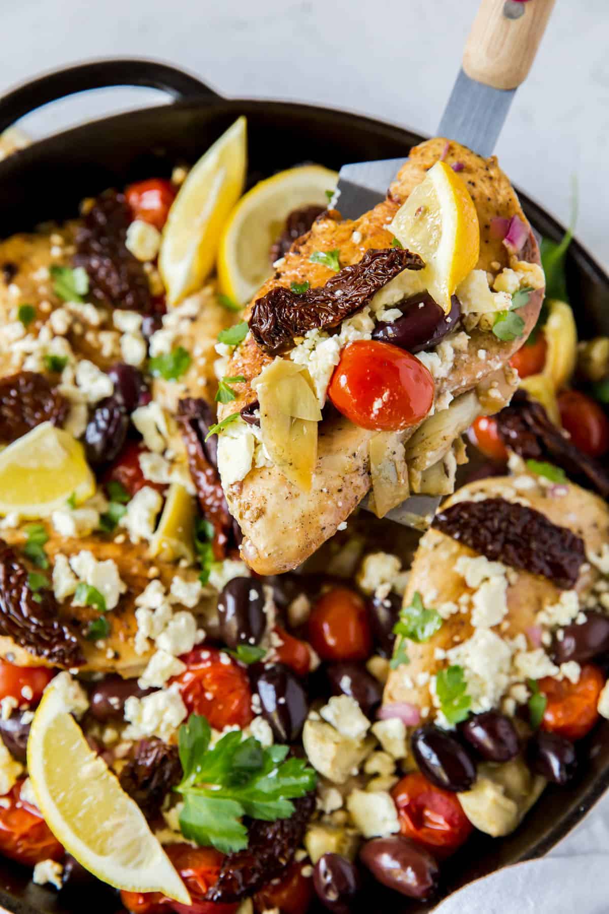 a piece of mediterranean chicken in a skillet with toppings