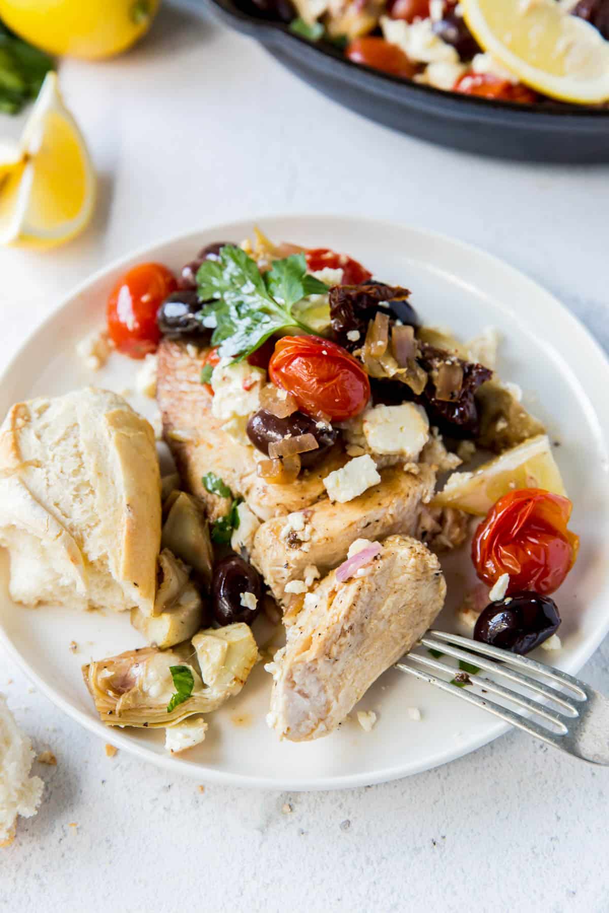 a piece of chicken on a plate with tomatoes, olives, feta and artichokes on top