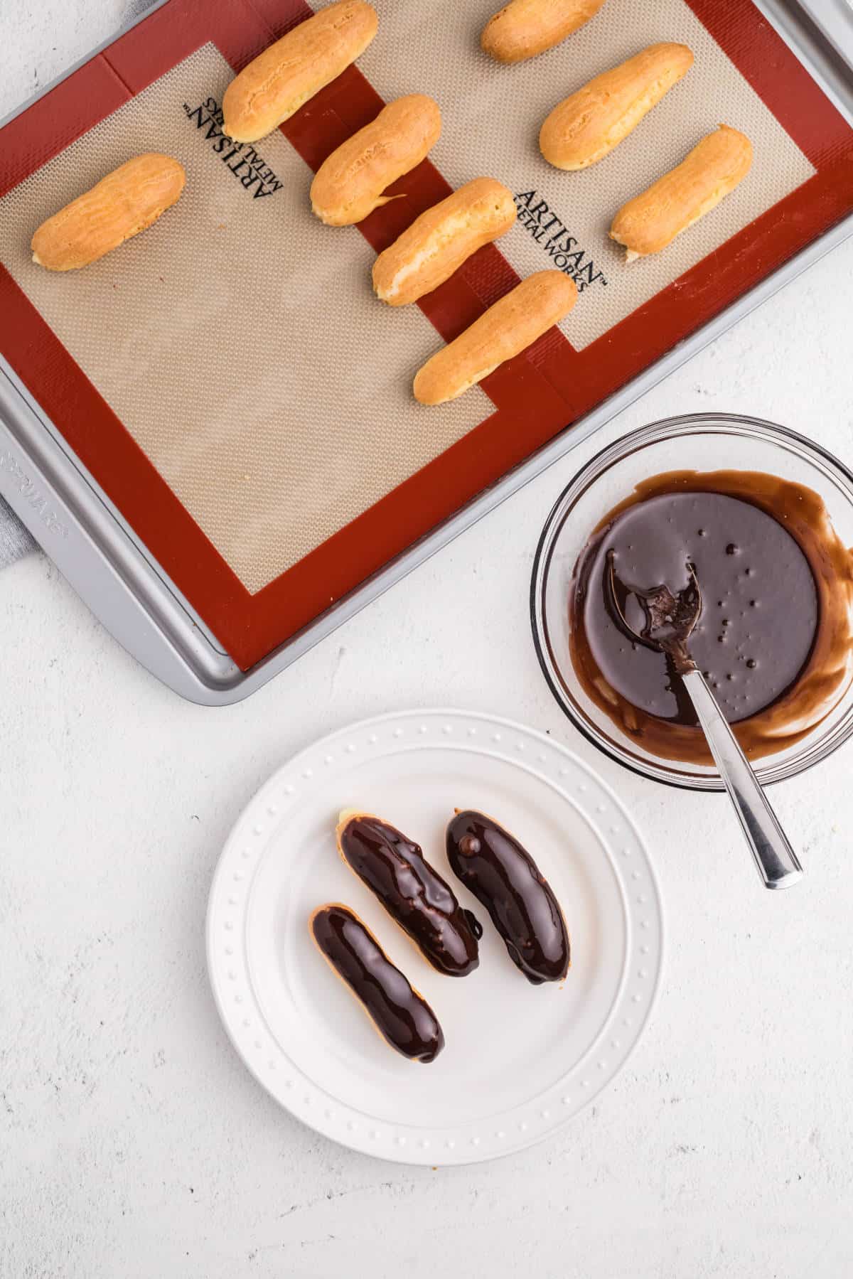 Filled eclairs being dipped into smooth chocolate glaze to coat the tops before serving.