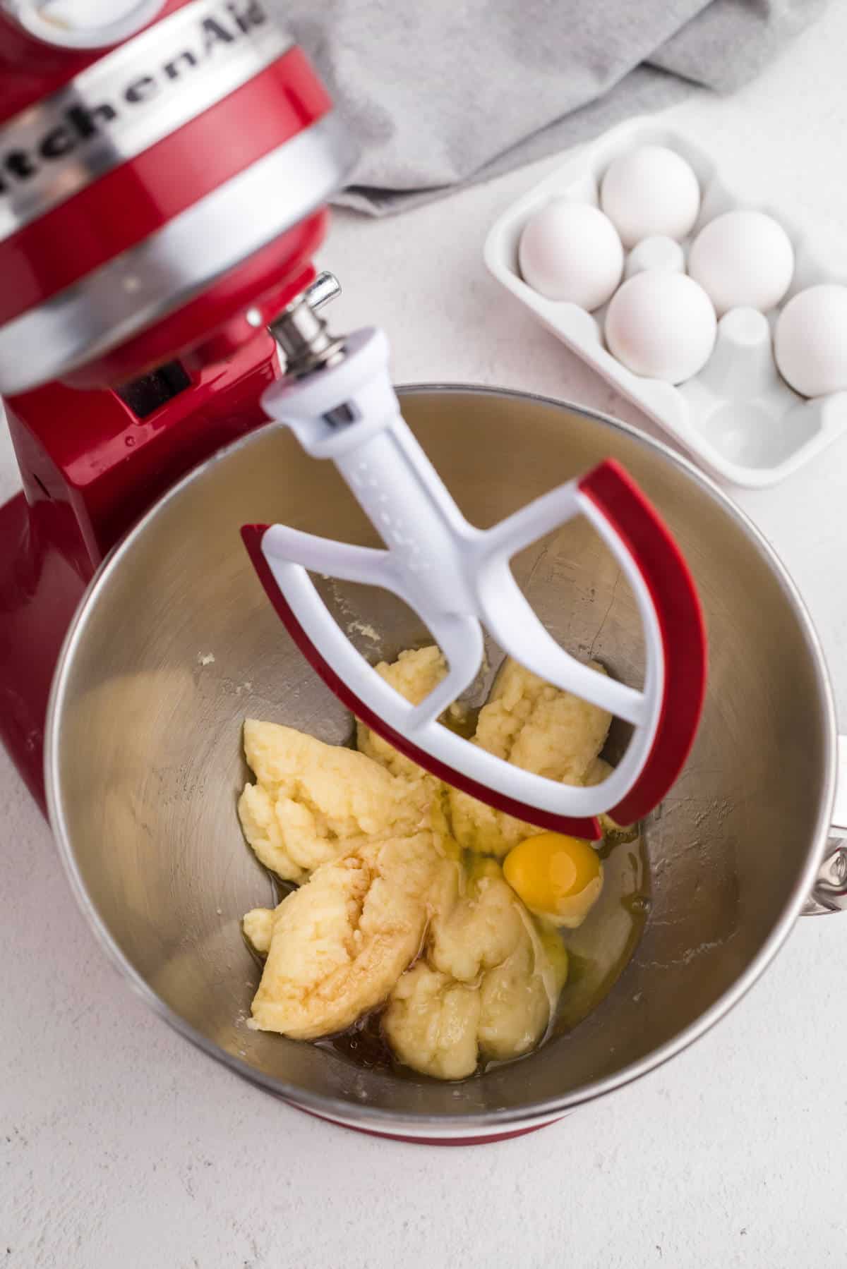 Choux pastry dough in a stand mixer with eggs being mixed in until smooth and glossy.