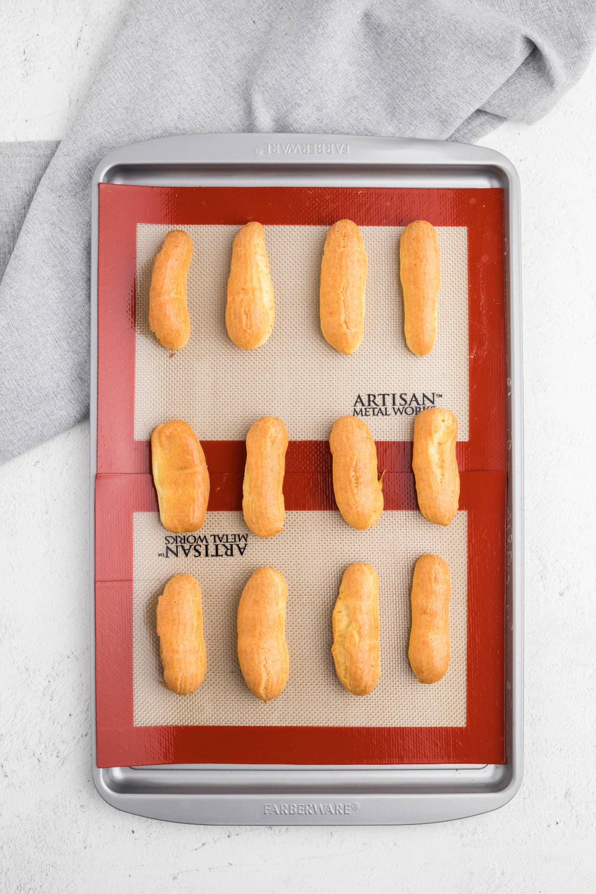 Baked choux pastry shells for eclairs, puffed and golden on a baking sheet.