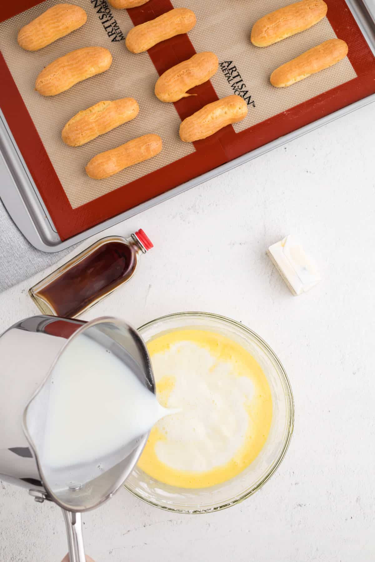 Hot milk being slowly poured into the egg and sugar mixture to temper the eggs for pastry cream.