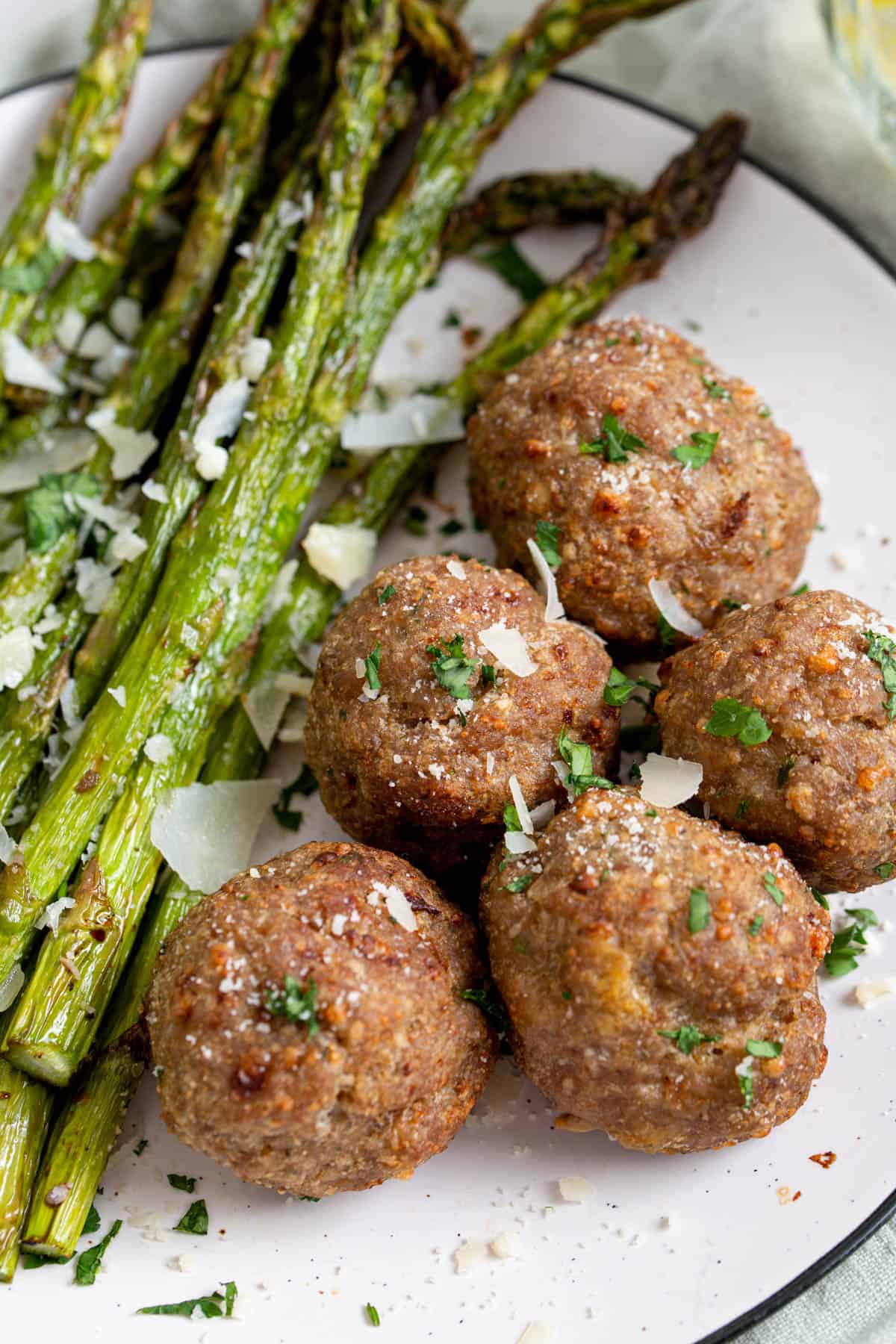 five turkey meatballs on a plate with cooked asparagus