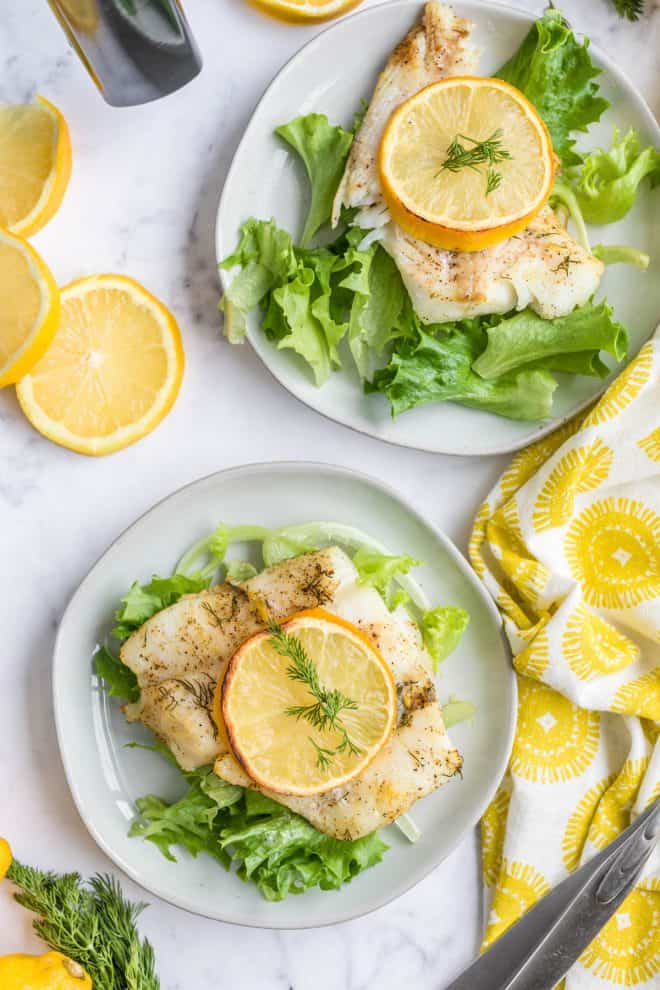 two slices of cod on plates with a slice of lemon on top of a bed of lettuce