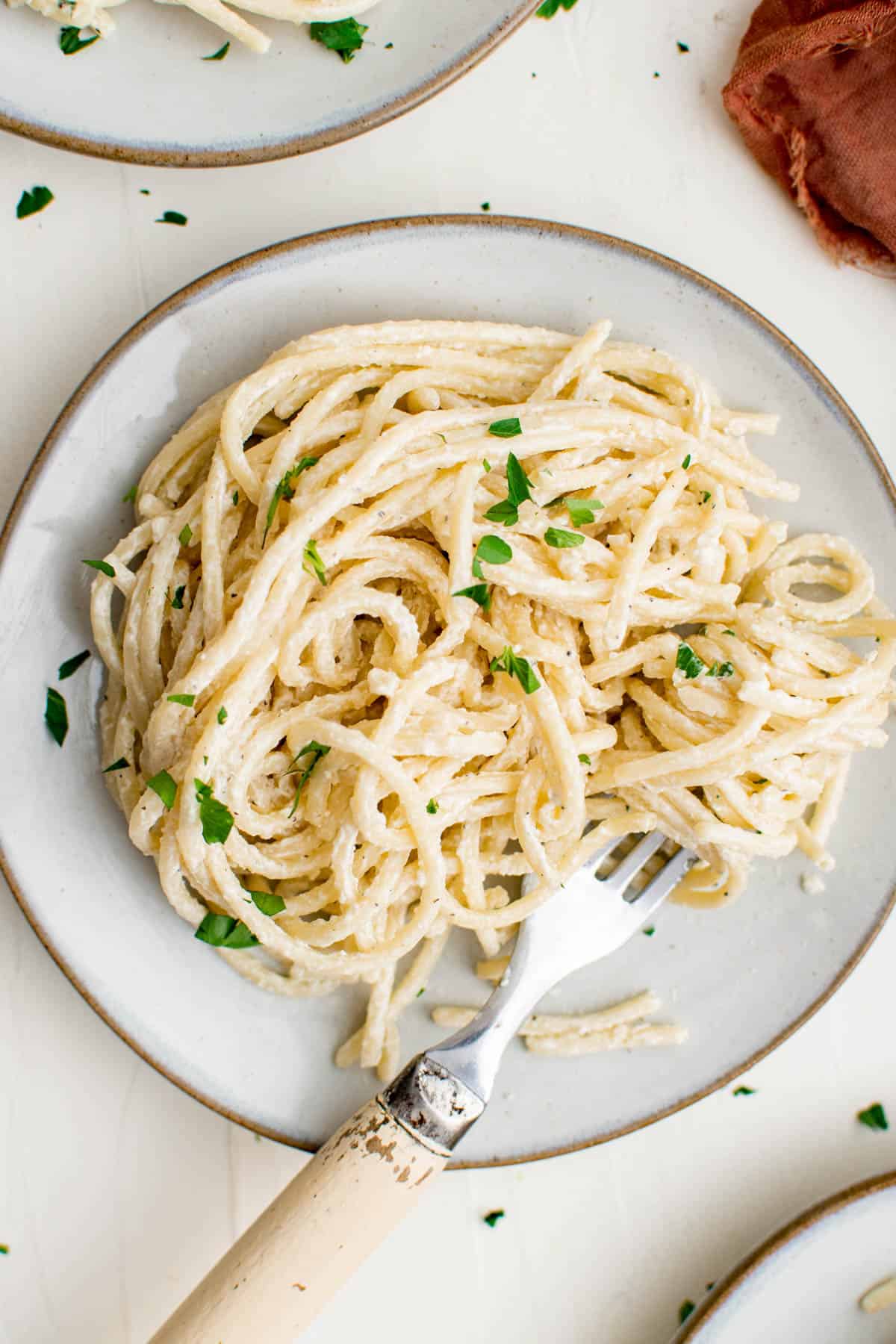 A plate of cream cheese pasta topped with parsley, and a silver fork