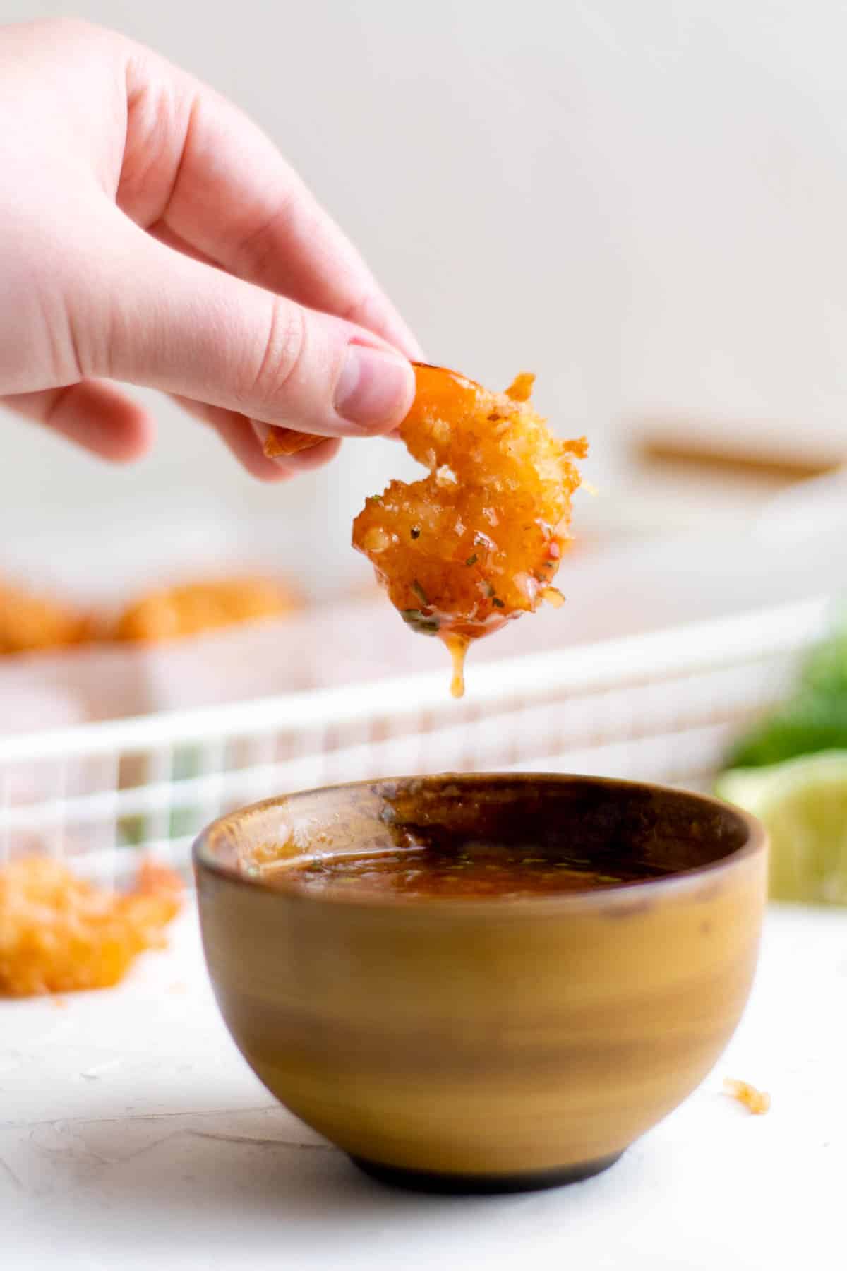 a hand dipping crispy coconut shrimp into a small bowl of sweet chili sauce