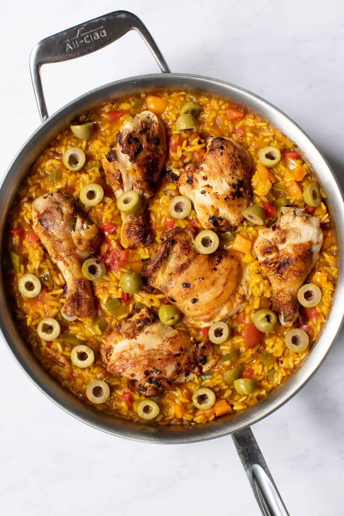 complete dish of spanish chicken and rice in a skillet with fresh olives on top