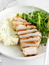 sliced bonless pork chop on a plate with arugula and mashed potatoes