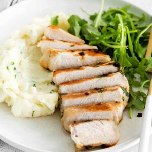 sliced bonless pork chop on a plate with arugula and mashed potatoes