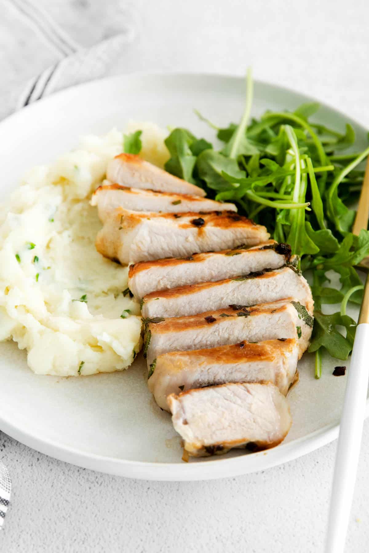 sliced bonless pork chop on a plate with arugula and mashed potatoes