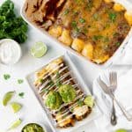 Aerial view of a pan of veggie enchiladas and a plate with two vegetable enchiladas, topped with guacamole and sour cream.