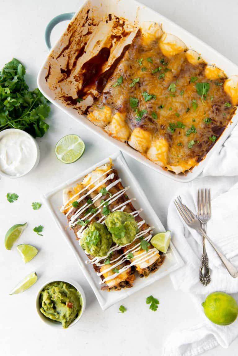 Aerial view of a pan of veggie enchiladas and a plate with two vegetable enchiladas, topped with guacamole and sour cream.