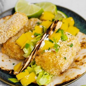 two air fryer fish tacos on a plate with fresh mango salsa on top