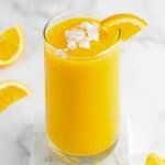 a glass of citrus smoothie with coconut flakes and sliced orange on top
