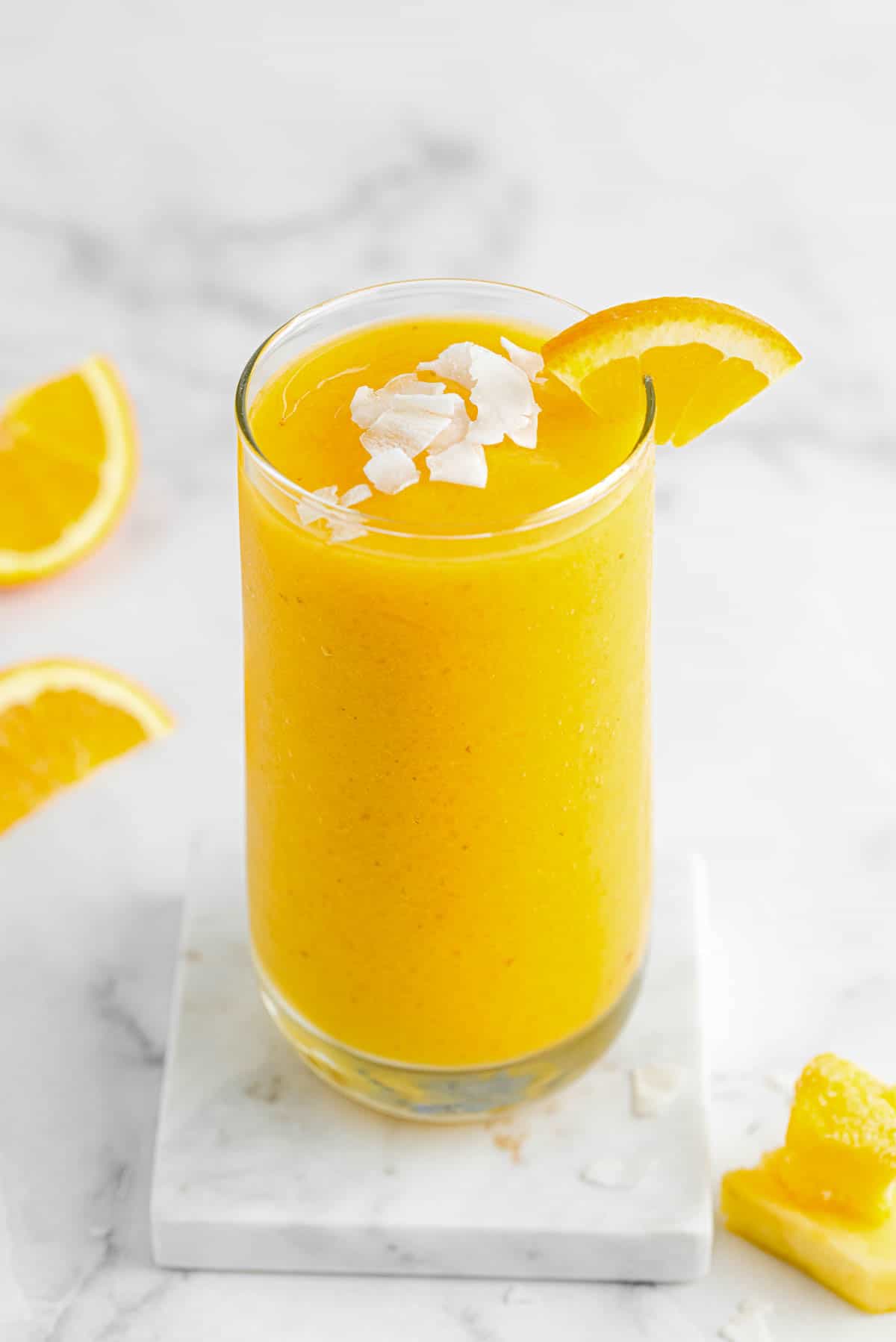 a glass of citrus smoothie with coconut flakes and sliced orange on top