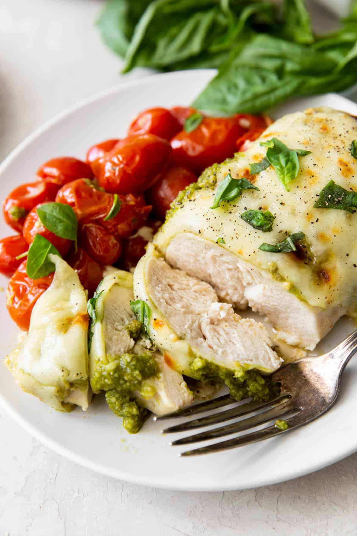 sliced pesto chicken on a plate with roasted tomatoes