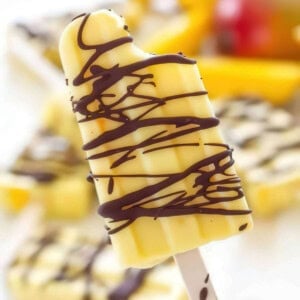 hand holding creamy mango popsicle drizzled with dark chocolate