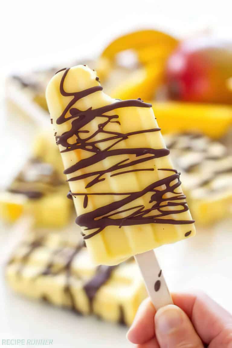 hand holding creamy mango popsicle drizzled with dark chocolate