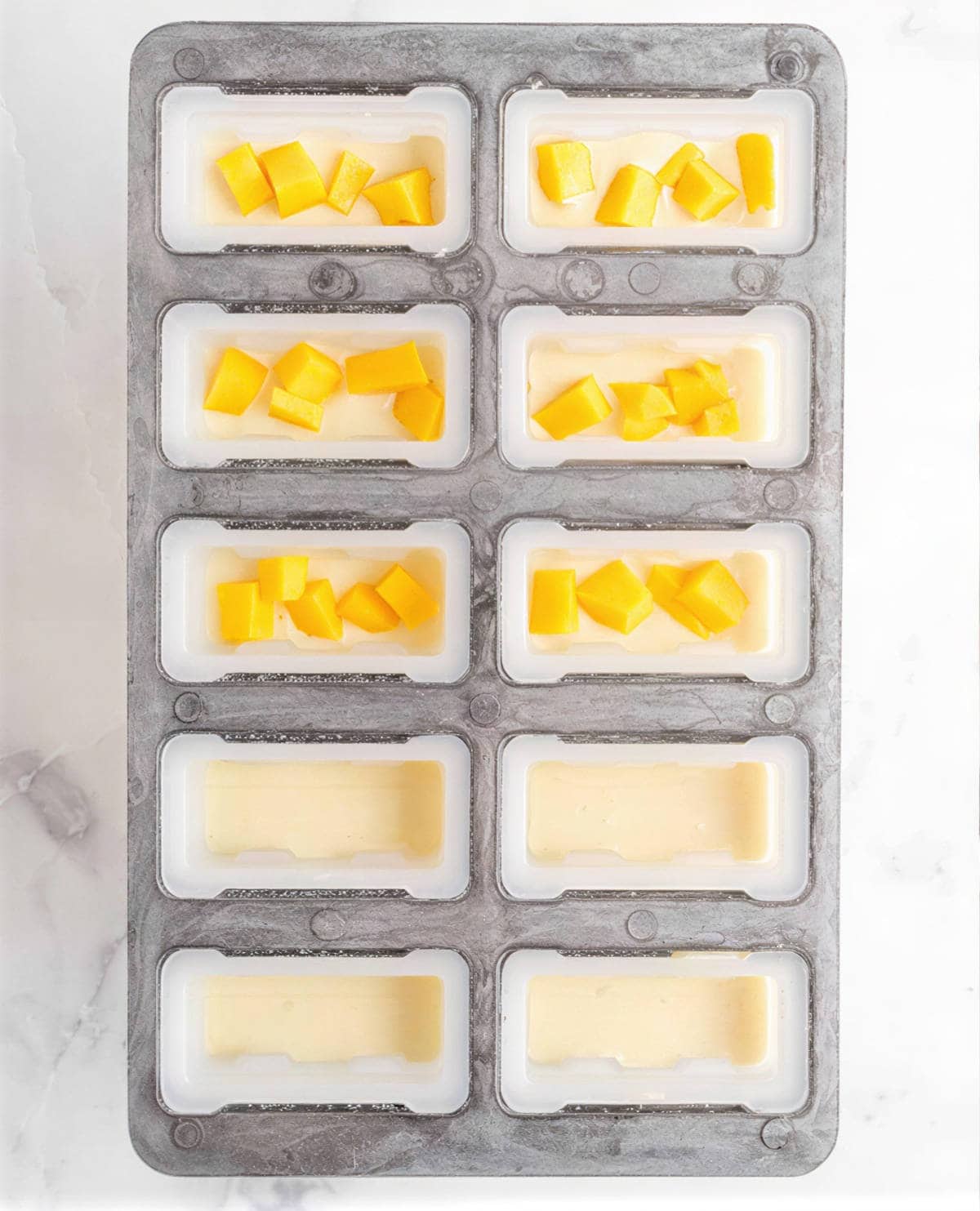 popsicle molds filled with creamy mango yogurt mixture and fresh mango pieces