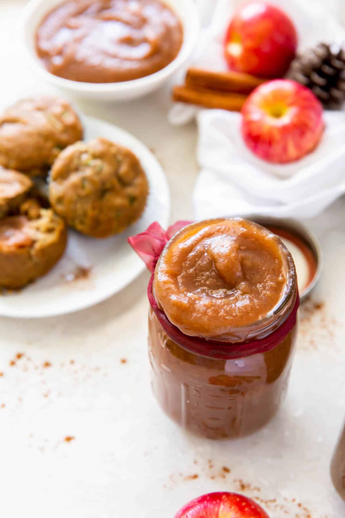 one jar of apple butter sitting on a counter next to a plate of muffins