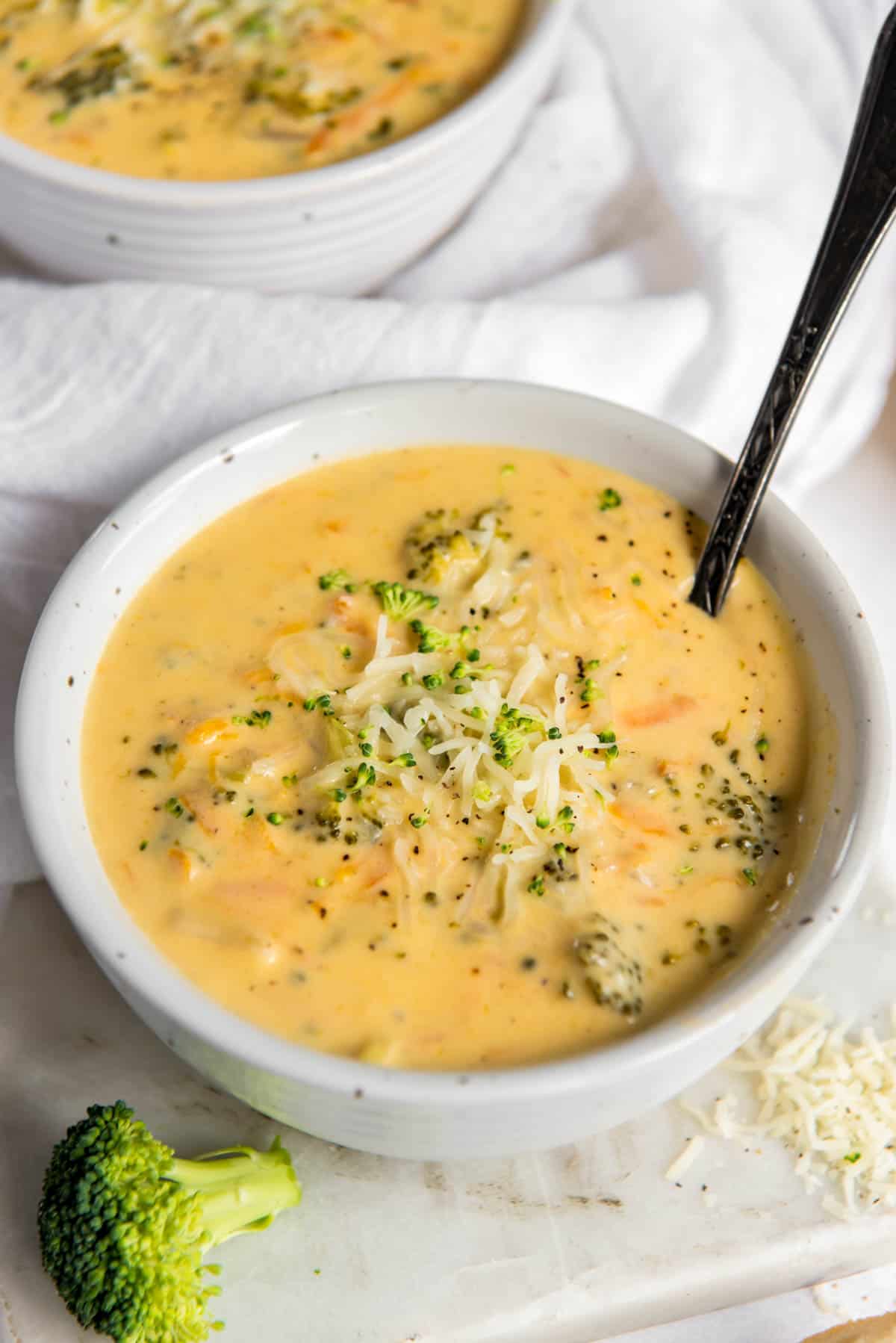one bowl filled with instant pot broccoli cheddar soup with a spoon in it