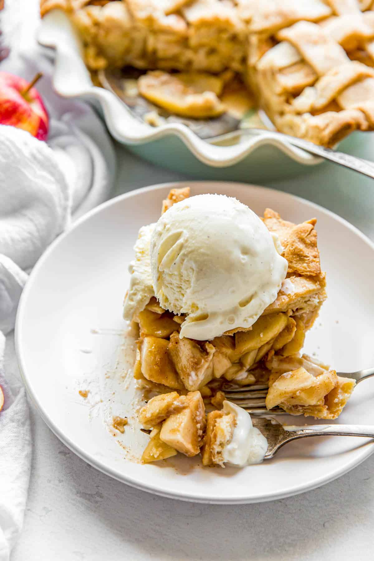 a slice of apple pie on a white plate with a scoop of vanilla ice cream on top