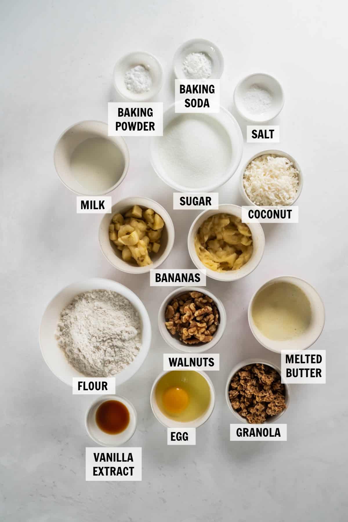 all of the ingredients for banana coconut muffins in bowls on a white countertop