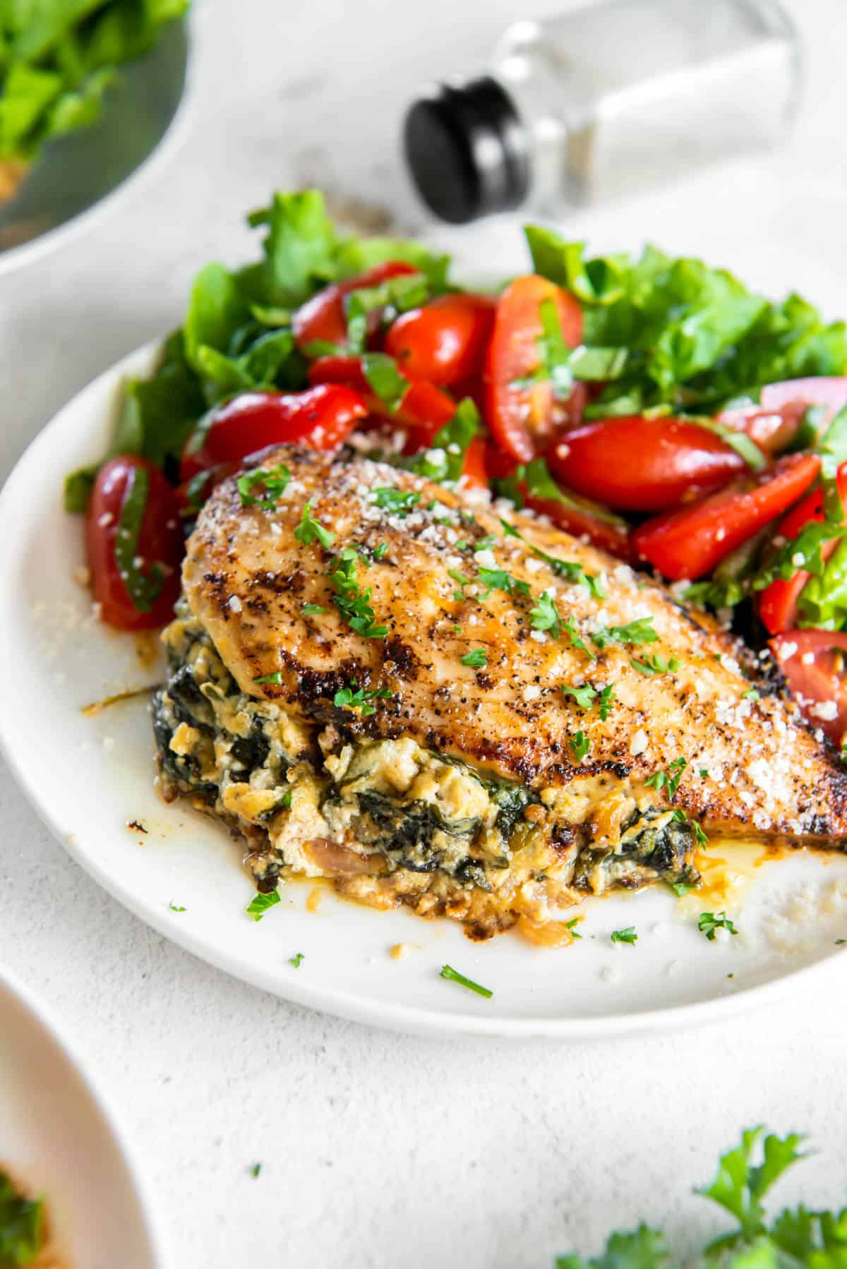 a white plate with spinach ricotta stuffed chicken and a fresh green salad