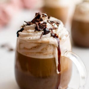 one mocha latter in a glass mug with whipped cream on top and chocolate drizzle