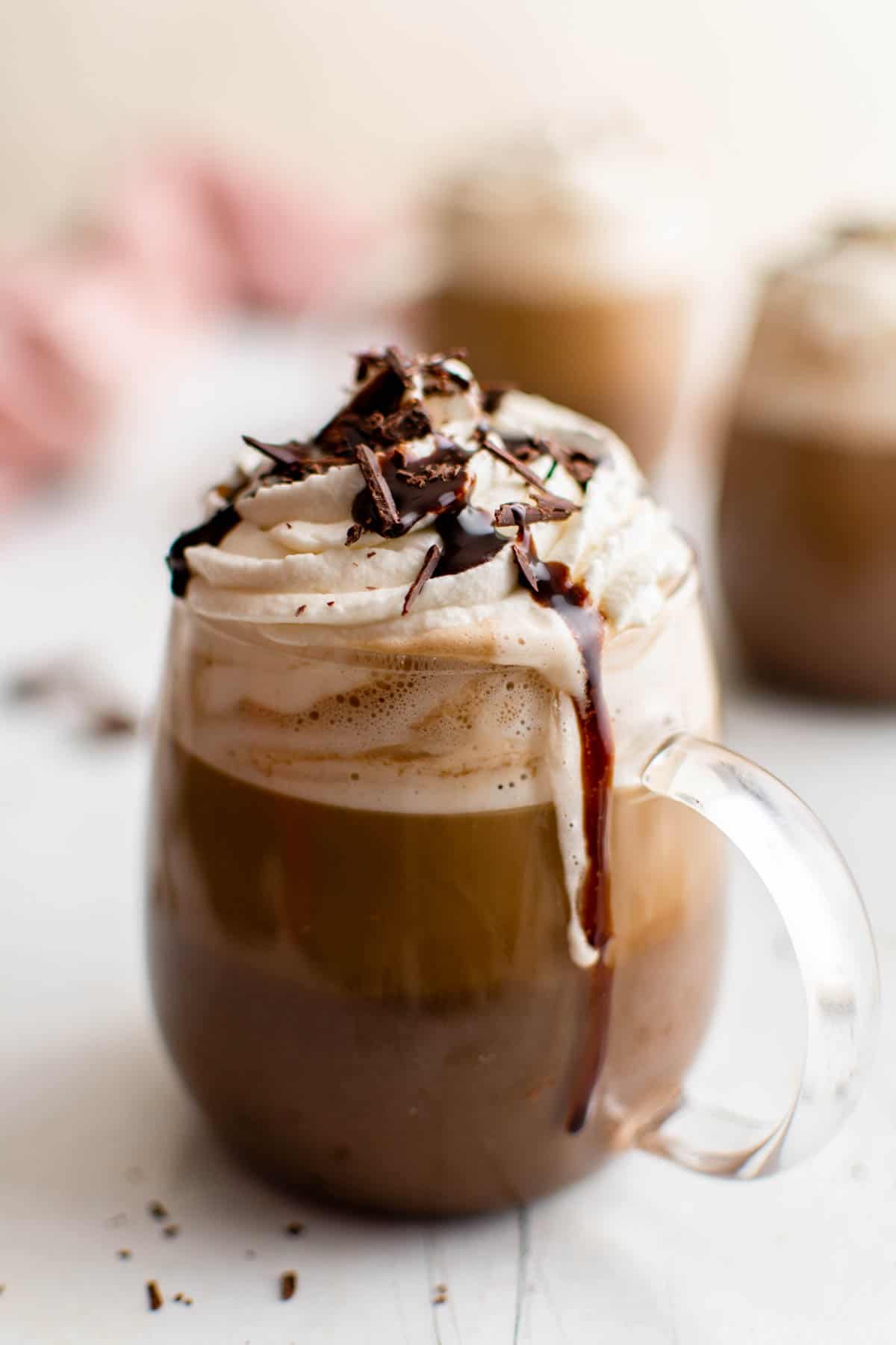 one mocha latter in a glass mug with whipped cream on top and chocolate drizzle