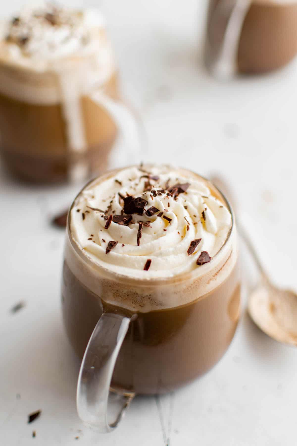 two mocha lattes in glass mugs with whipped cream on top